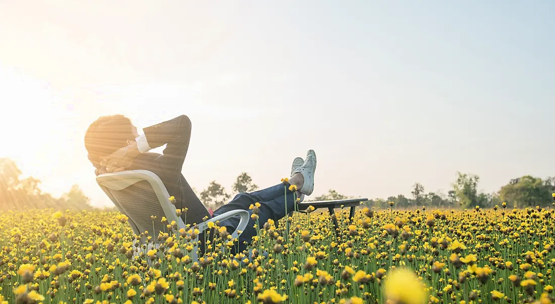 Businessman sitting in office armchair and relaxing in yellow flower field.