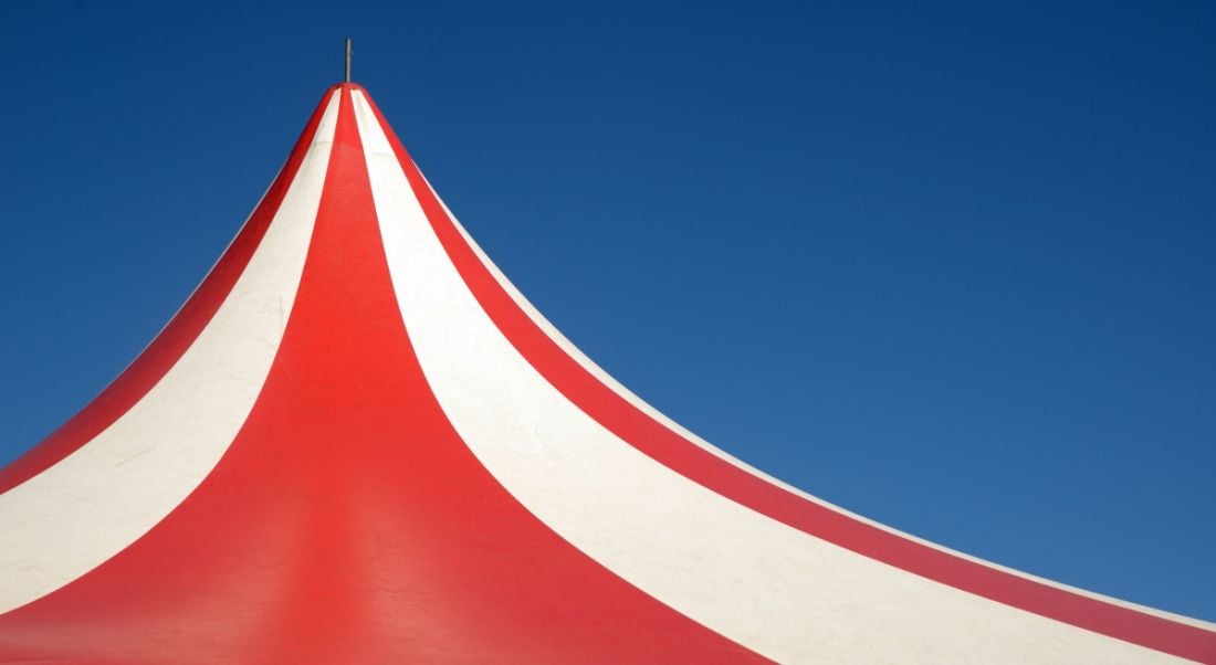 Red and white striped circus tent against a blue sky.