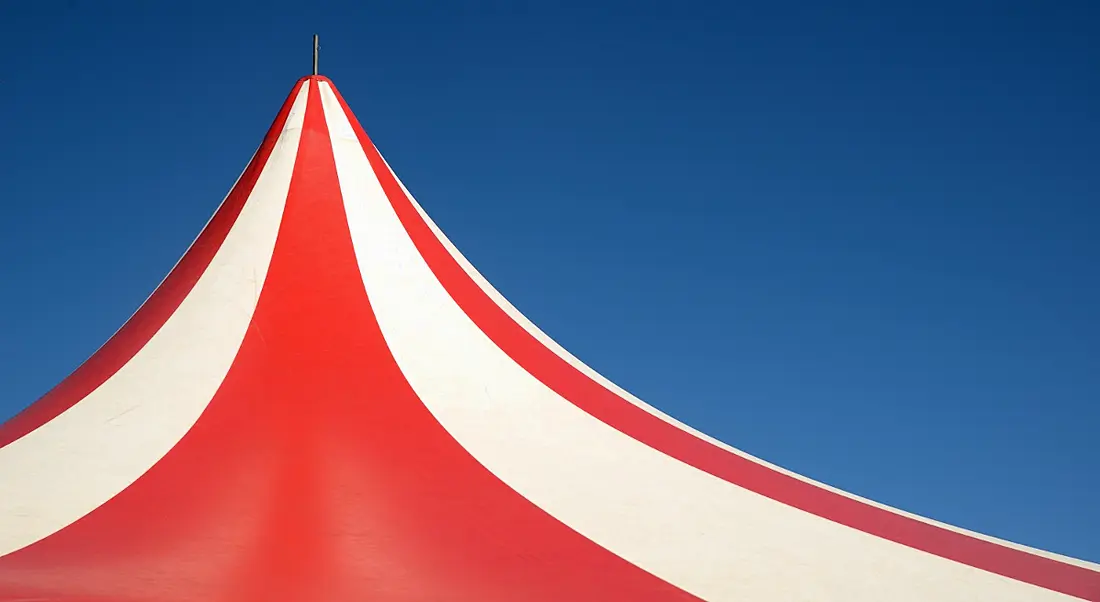 Red and white striped circus tent against a blue sky.