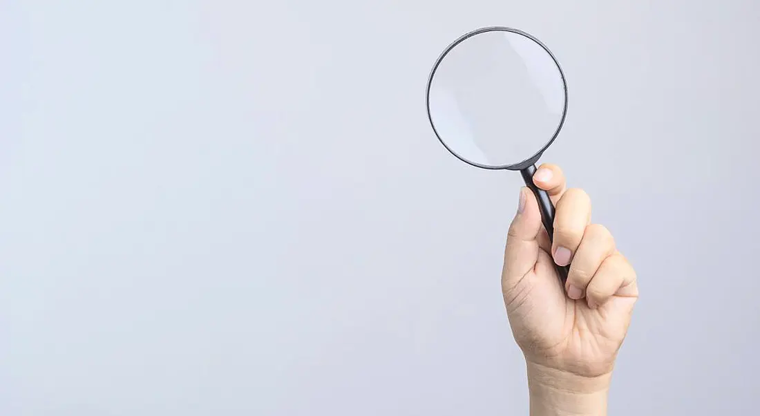 Hand holding magnifying glass on white background.