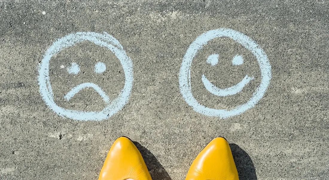 Tips of yellow shoes on gravel pointing to a smiley face and a sad face drawn in chalk.