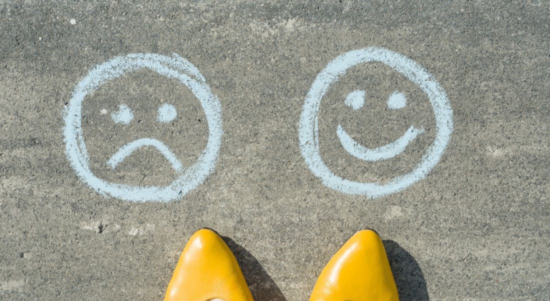 Tips of yellow shoes on gravel pointing to a smiley face and a sad face drawn in chalk.