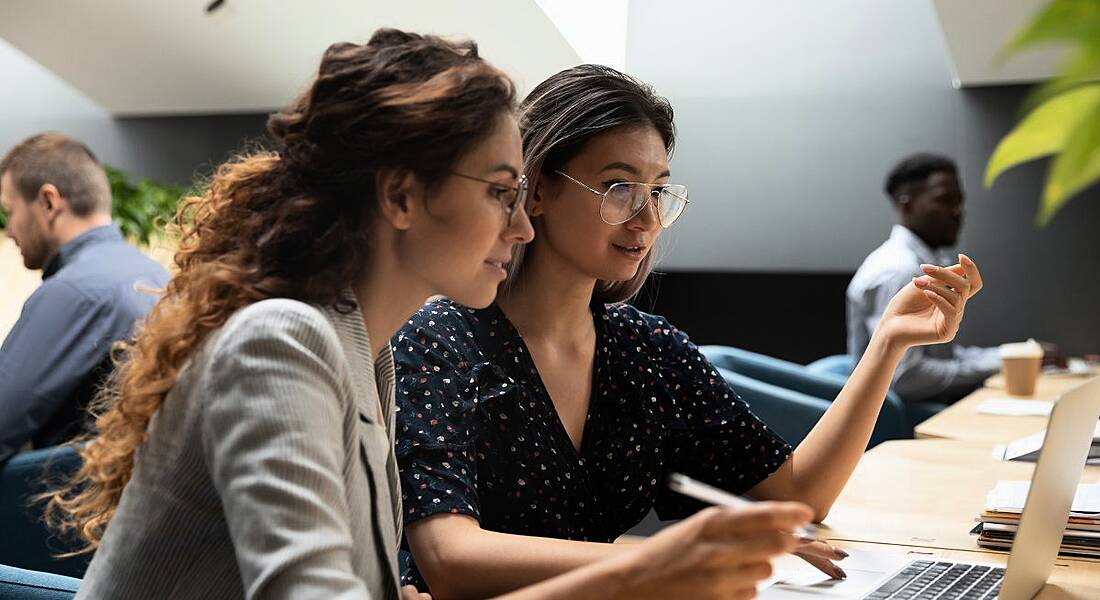 Two women are sitting and collaborating at a laptop