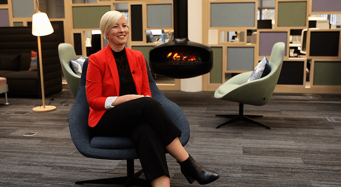 A woman is sitting on a chair in an office setting by a stove fire.