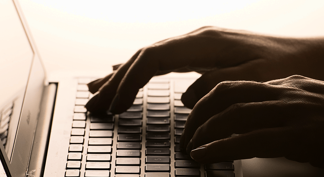 Hands typing on the keyboard of a laptop.