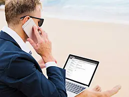 Laptop, mobile phone, tablet and documents on a working table in an office setting, with colleagues sitting around it.