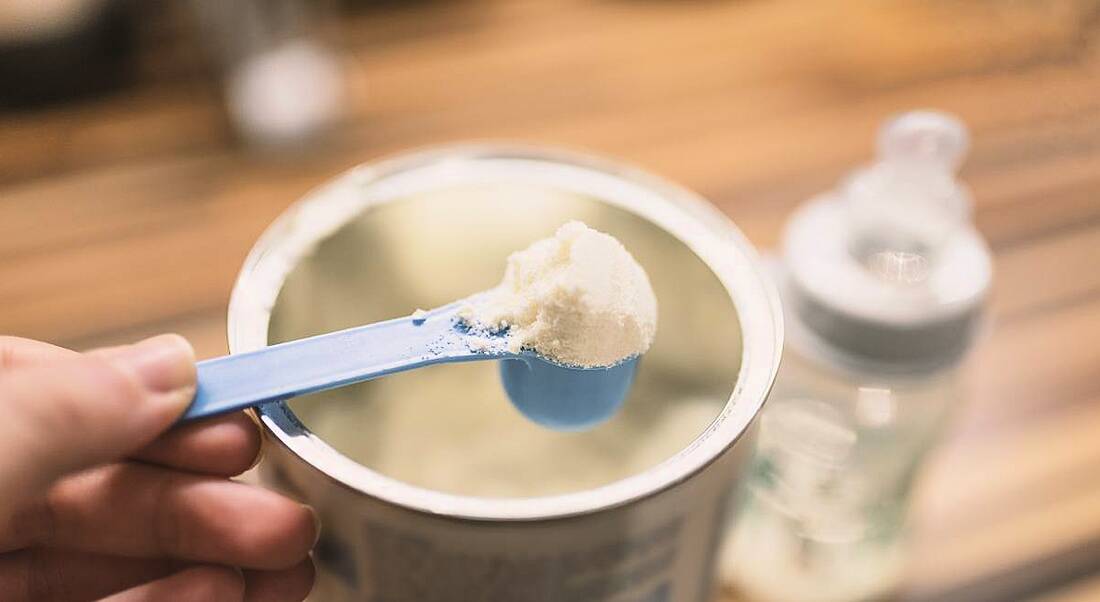 Powder milk for baby and blue spoon on light background close-up.