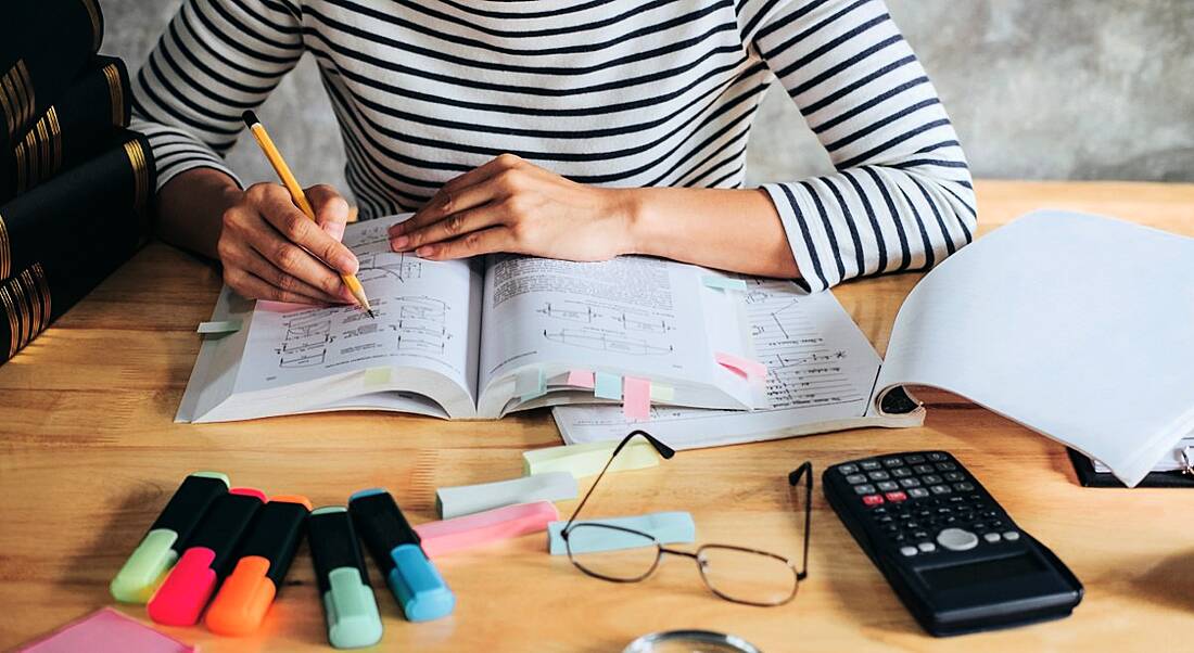 Young student sitting at desk in home studying and reading for science degree.