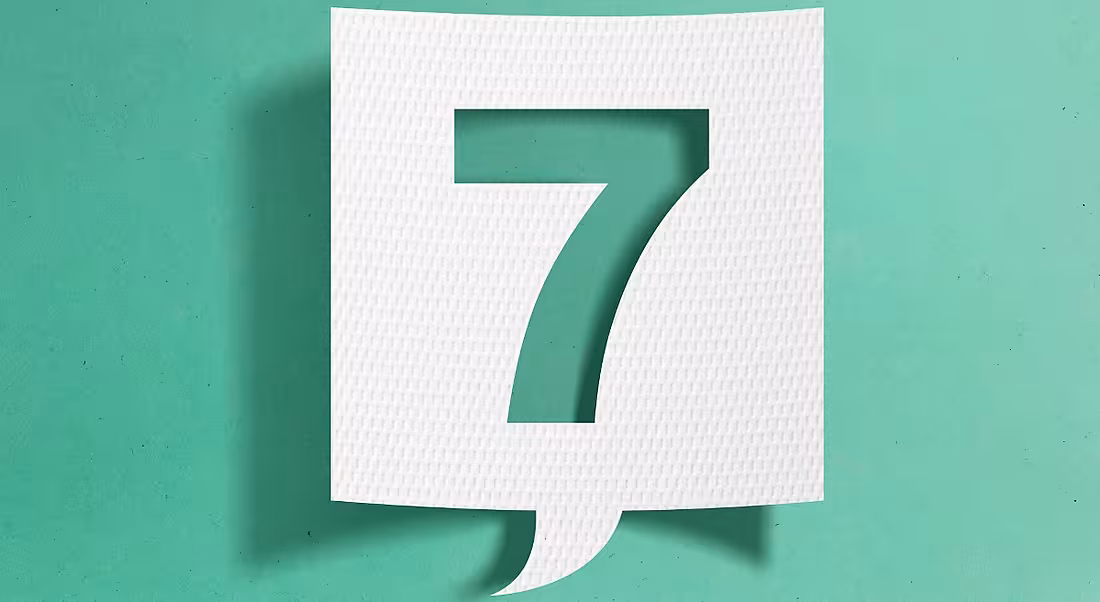 A slip of white paper cut into the shape of a speech bubble, with the number seven cut out from the centre, on a turquoise background.