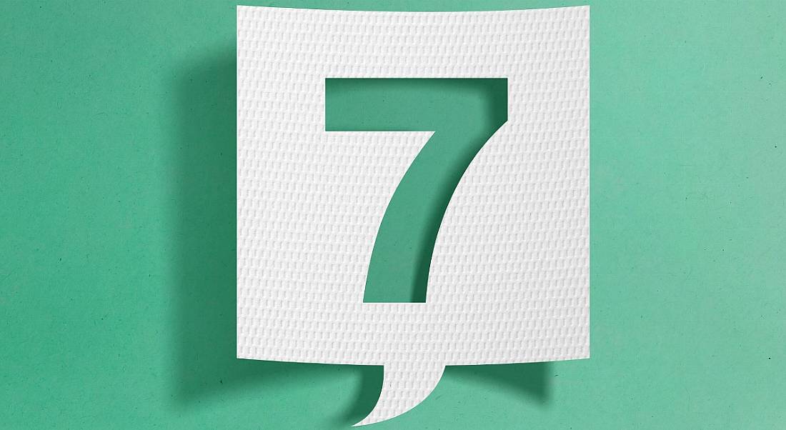 A slip of white paper cut into the shape of a speech bubble, with the number seven cut out from the centre, on a turquoise background.