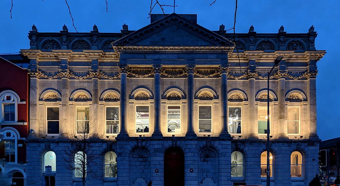 The Eventbrite office in Cork is a large grey building, lit up at its front against a night sky.