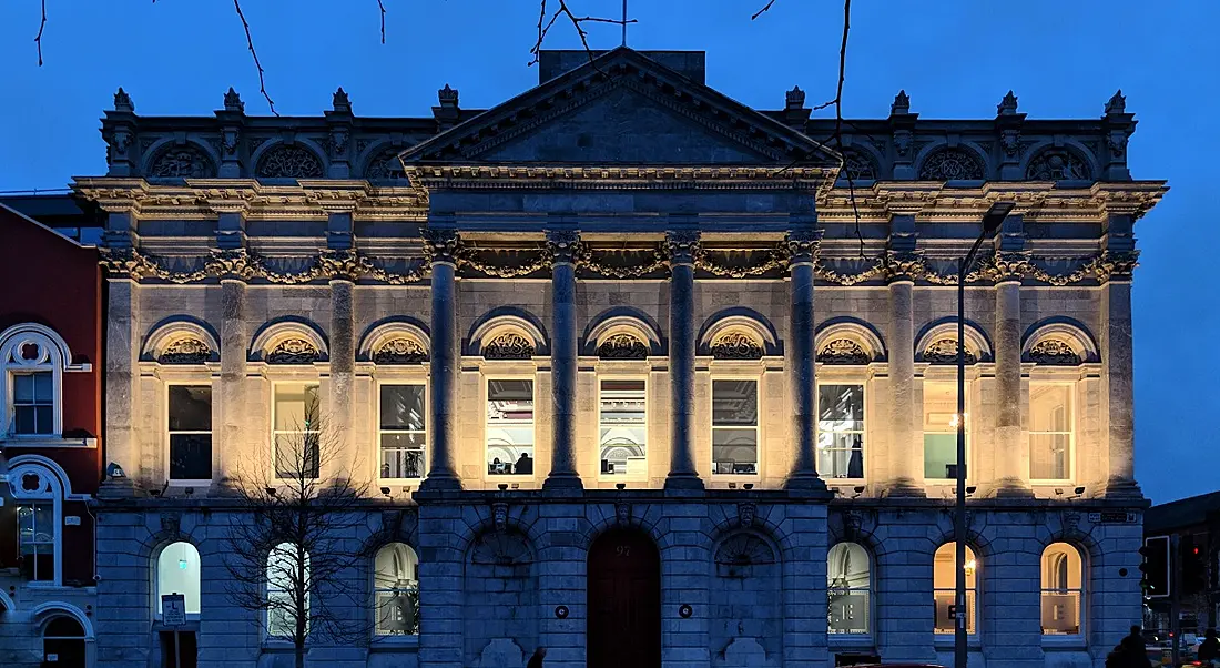 The Eventbrite office in Cork is a large grey building, lit up at its front against a night sky.