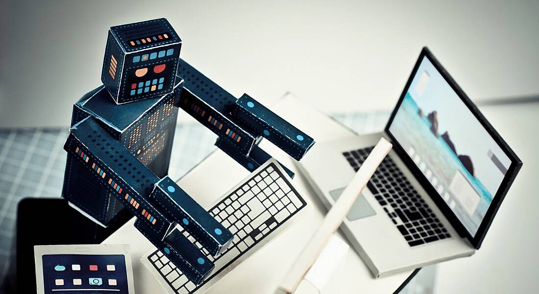 A toy robot is working on a laptop at an office desk.