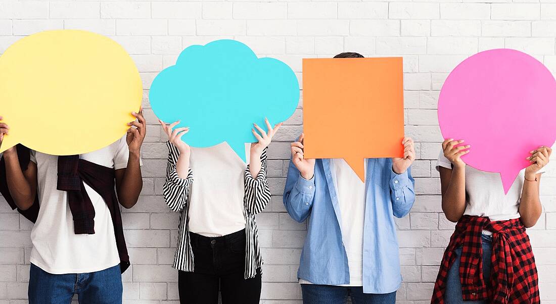 Teenagers holding different coloured and shaped speech bubbles, standing against a white wall.