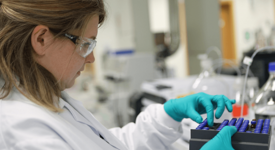 A woman is working in a lab setting, wearing a lab coat and safety goggles, at MSD Ballydine.