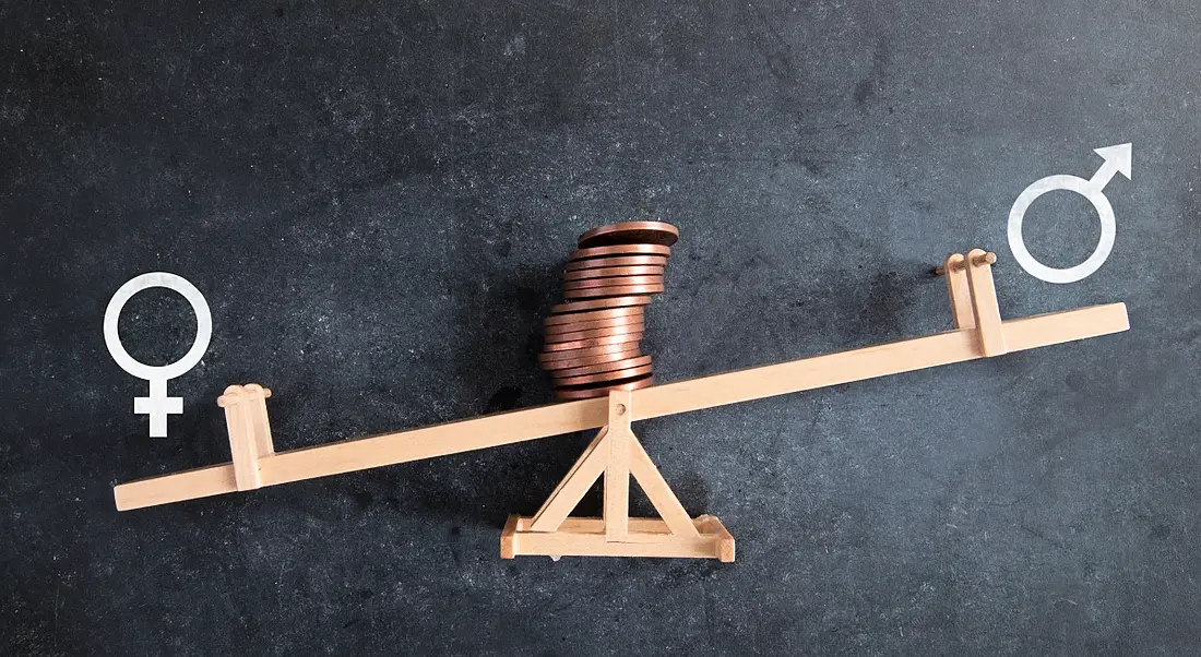 Chalkboard graph illustrating and upward line graph unequal pay bias towards men with stack of coins resting on top of a seesaw.