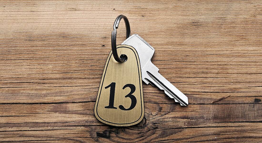 Close-up of a key with a tag reading the number 13, sitting on a wooden desk.