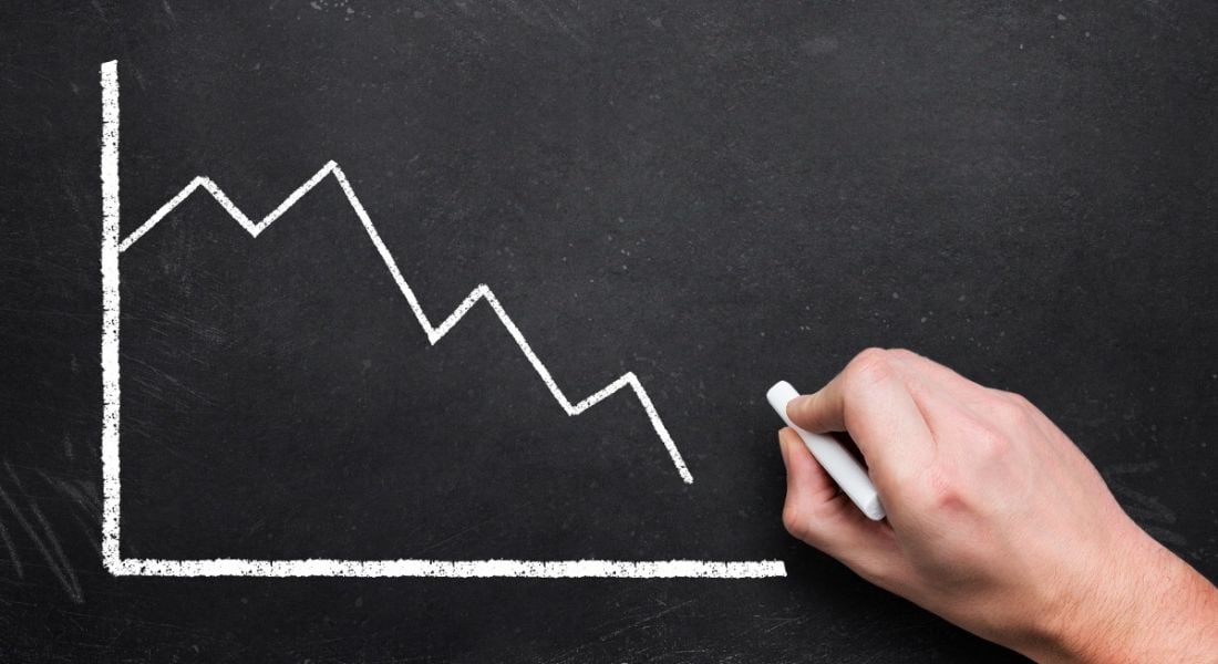 A white graph is being drawn on a blackboard in chalk, with the trend falling downwards.