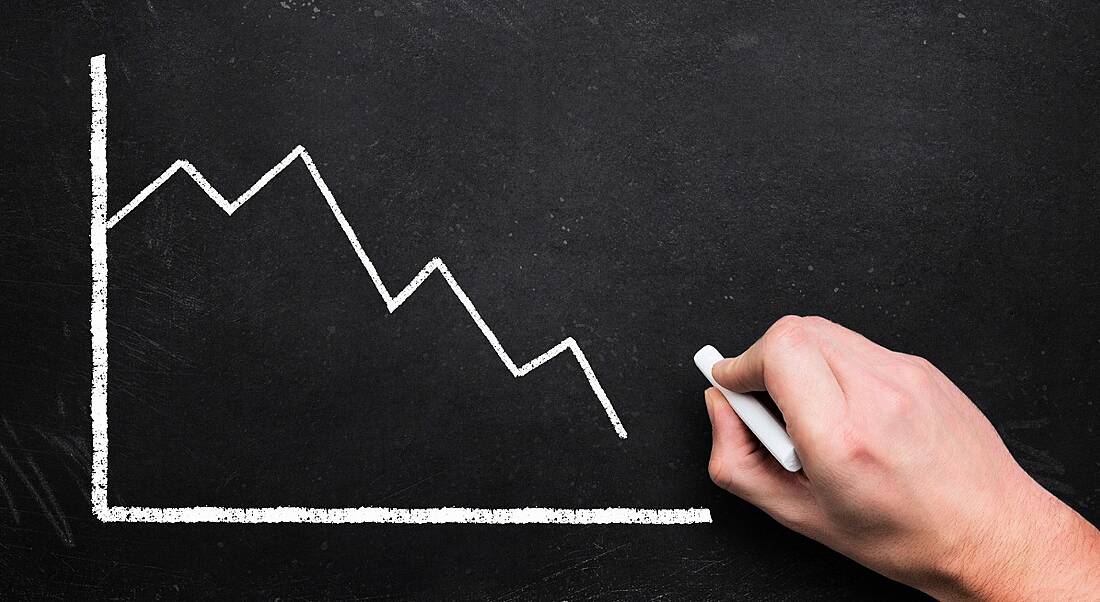 A white graph is being drawn on a blackboard in chalk, with the trend falling downwards.