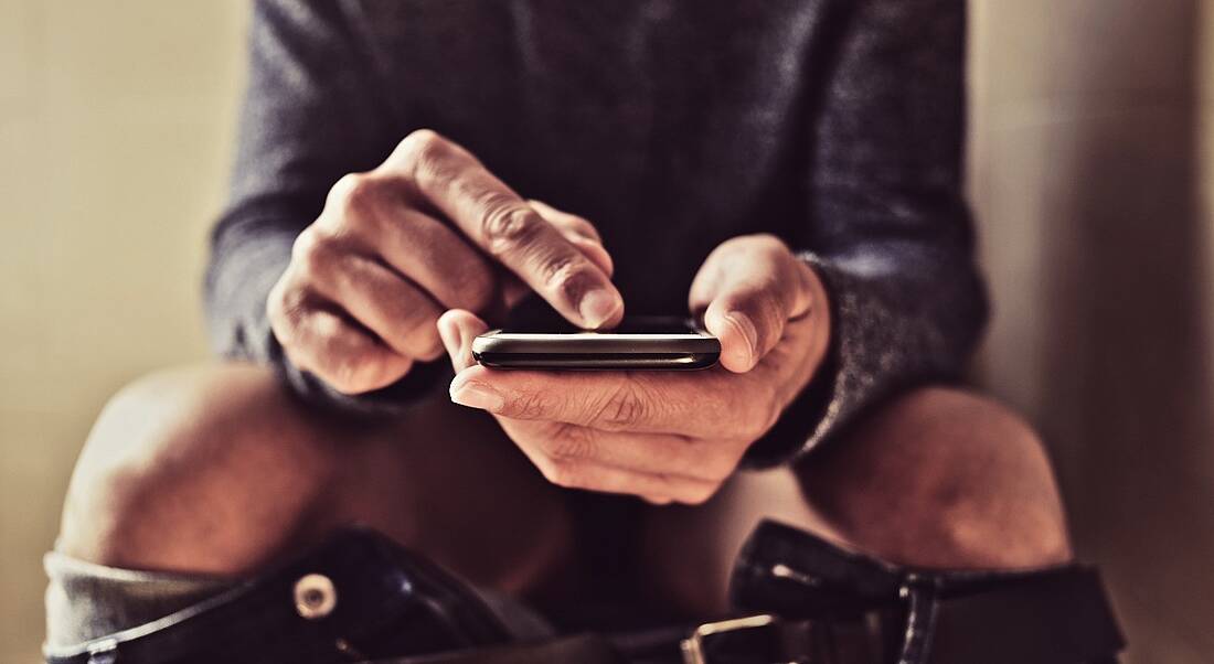 A man using his smartphone while sitting on the toilet.