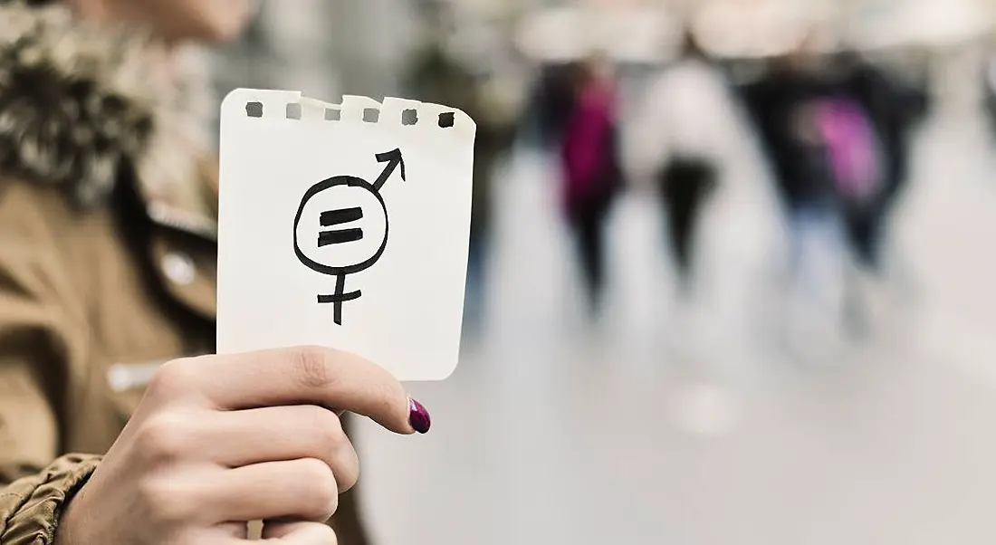 Close-up of a person's hand in the street, showing a piece of paper with a symbol for gender equality drawn on it.