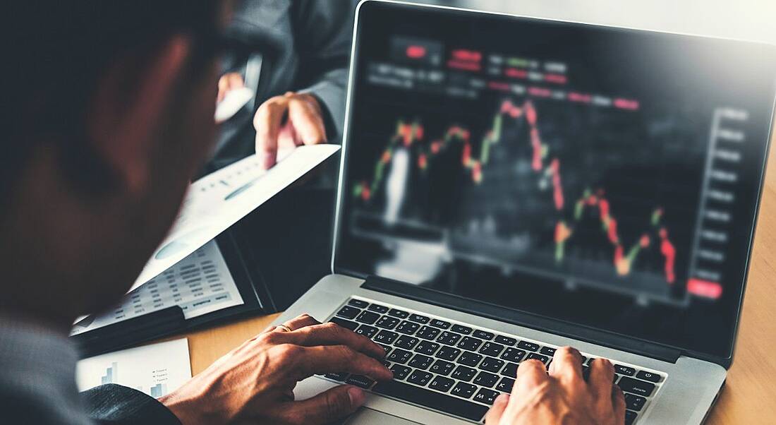 A professional man is typing on a laptop that has charts and graphs on the screen, representing data analytics work.