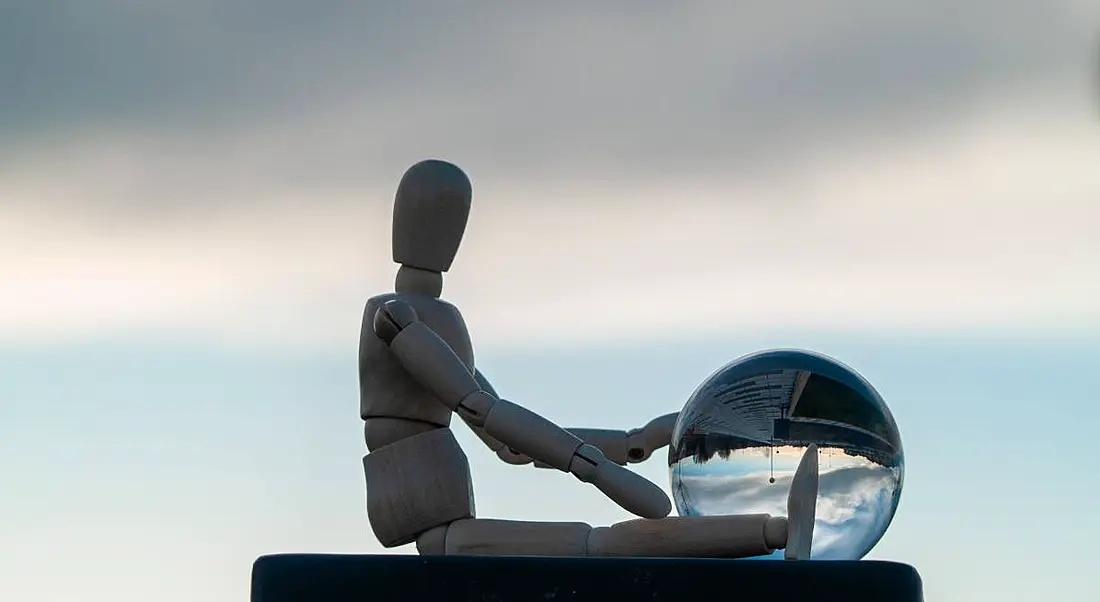 Wooden mannequin sitting against a sky backdrop with a crystal ball.