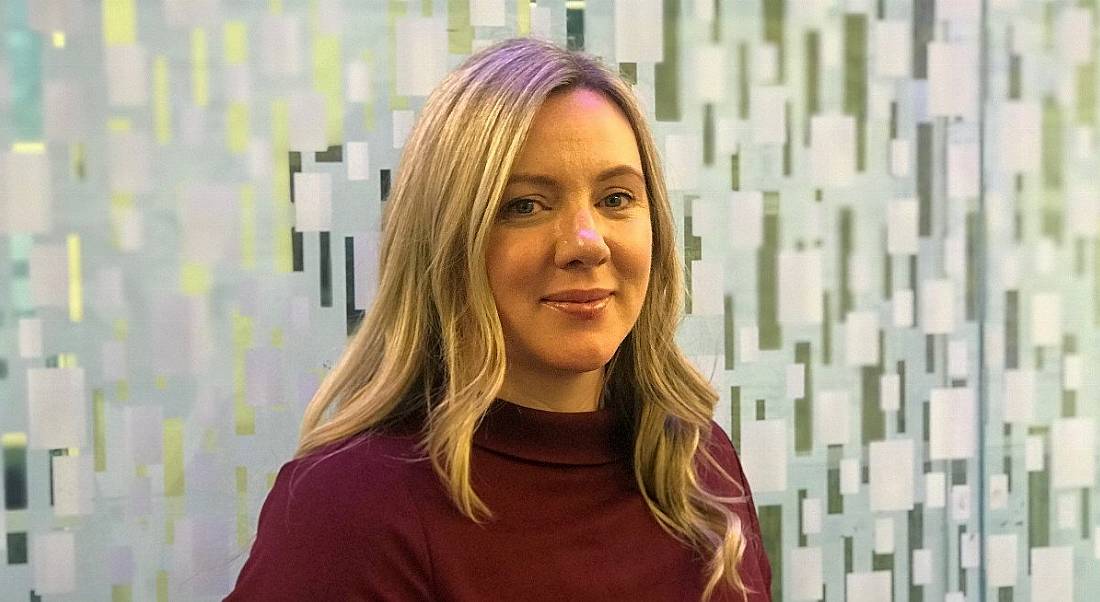 A professional woman is smiling into the camera with blonde hair and a red dress, standing in the Dublin office of Citi.