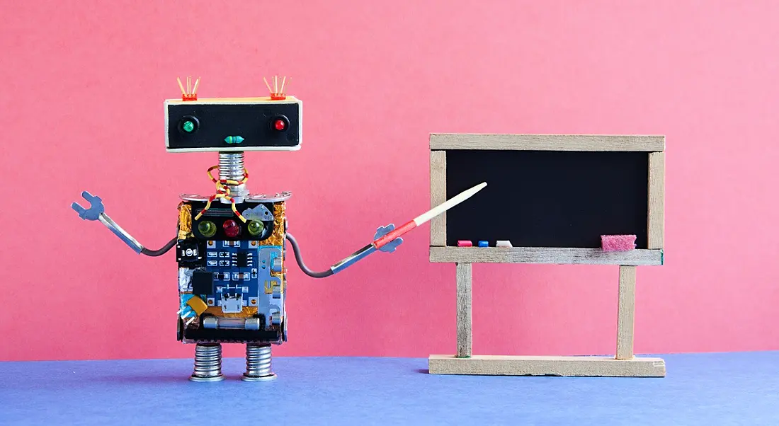 A toy robot is teaching using a blackboard in a colourful classroom setting.