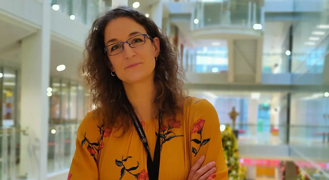 A professional woman is looking into the camera in a brightly lit office space at Mastercard.