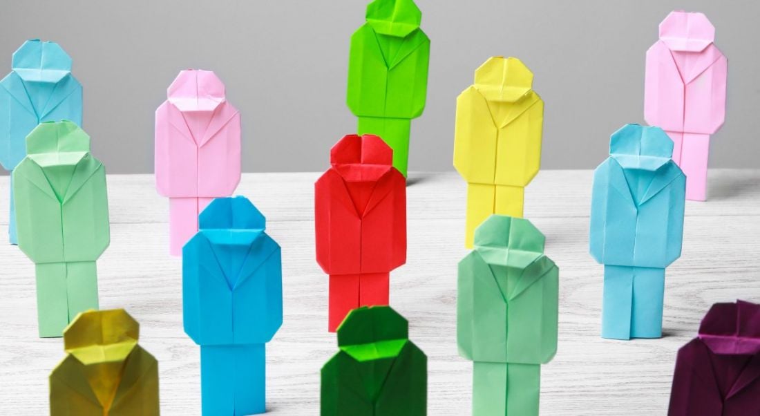 Paper figurines made out of colourful paper. They are all arranged on a white table on a white background.