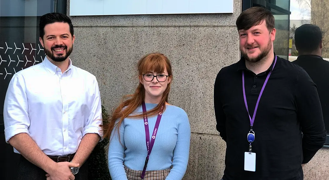 Two men and a woman stand smiling in front of a wall. They are Rory West, Amy McGuire and Alan Sorohan, all employees at Viatris.