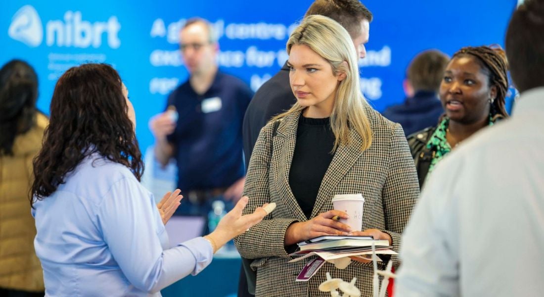 Two women in focus in a crowded room at the NIBRT biopharma careers fair in Ireland talking to each other.