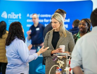 Two women in focus in a crowded room at the NIBRT biopharma careers fair in Ireland talking to each other.