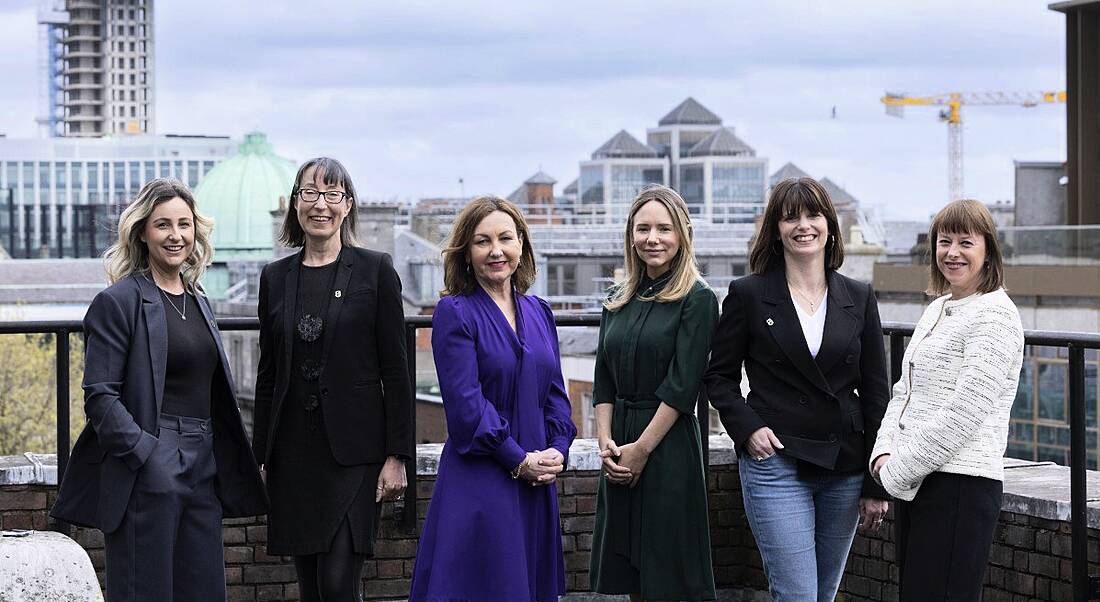 A wide shot of six women at the Guaranteed Irish tech forum panel on the roof a building with the Dublin skyline and a cloudy sky in the background.