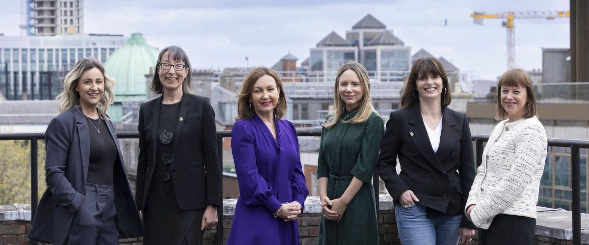 A wide shot of six women at the Guaranteed Irish tech forum panel on the roof a building with the Dublin skyline and a cloudy sky in the background.