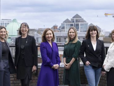 A wide shot of six women at the Guaranteed Irish tech forum panel on the roof a building with the Dublin skyline and a cloudy sky in the background.