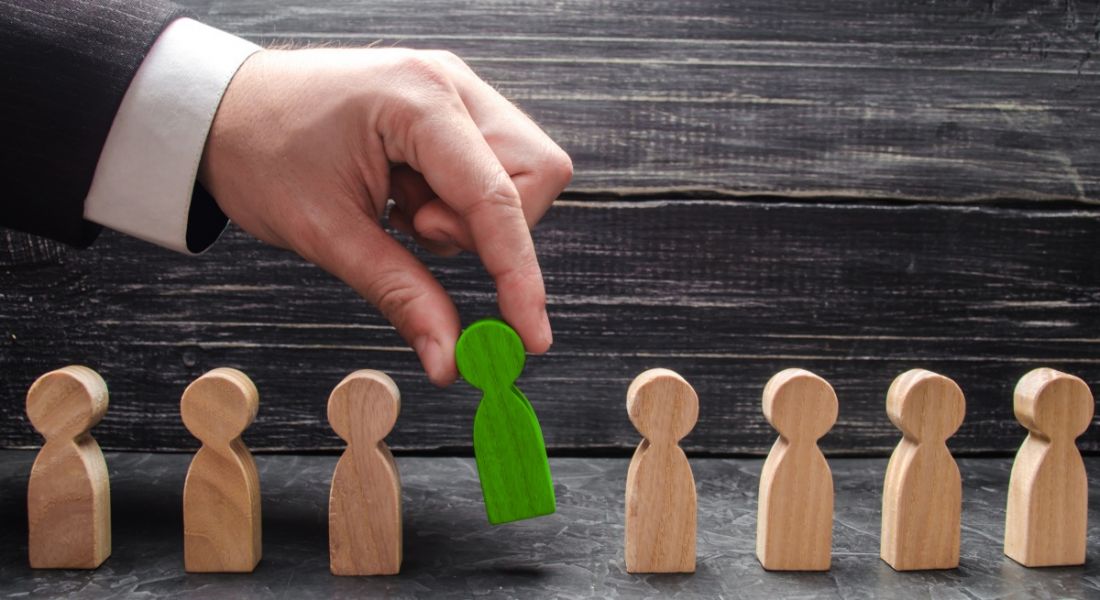 A businessperson selects a green figure from lineup of unpainted figures, representing process of job application and selection.