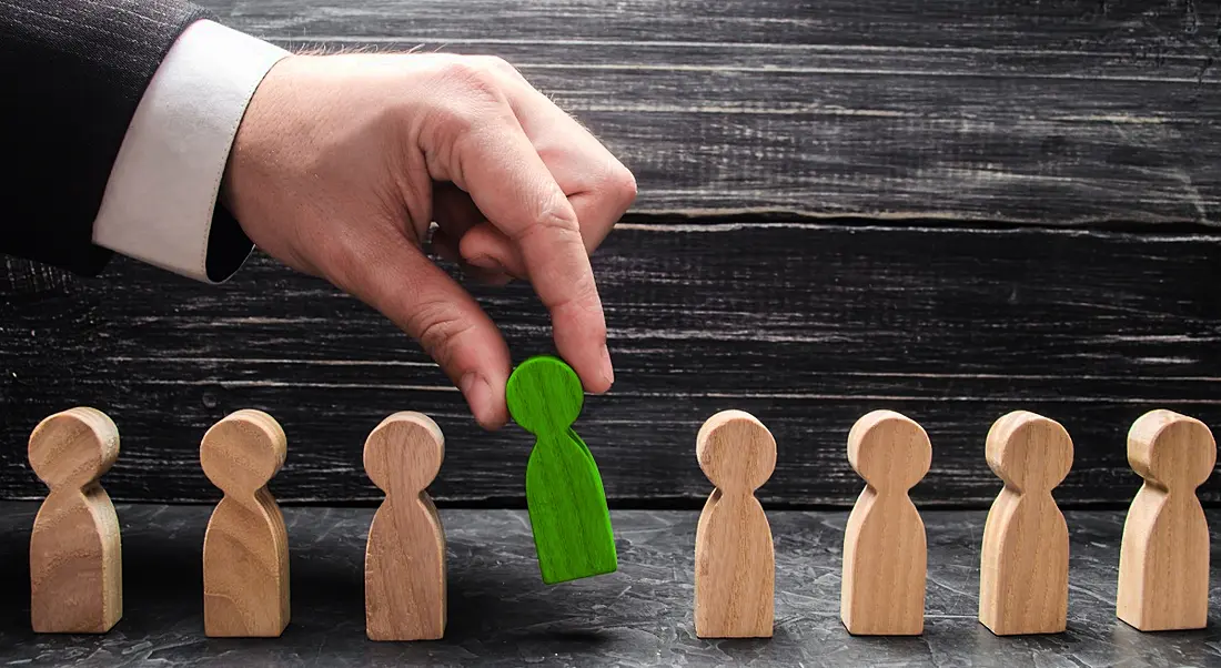 A businessperson selects a green figure from lineup of unpainted figures, representing process of job application and selection.