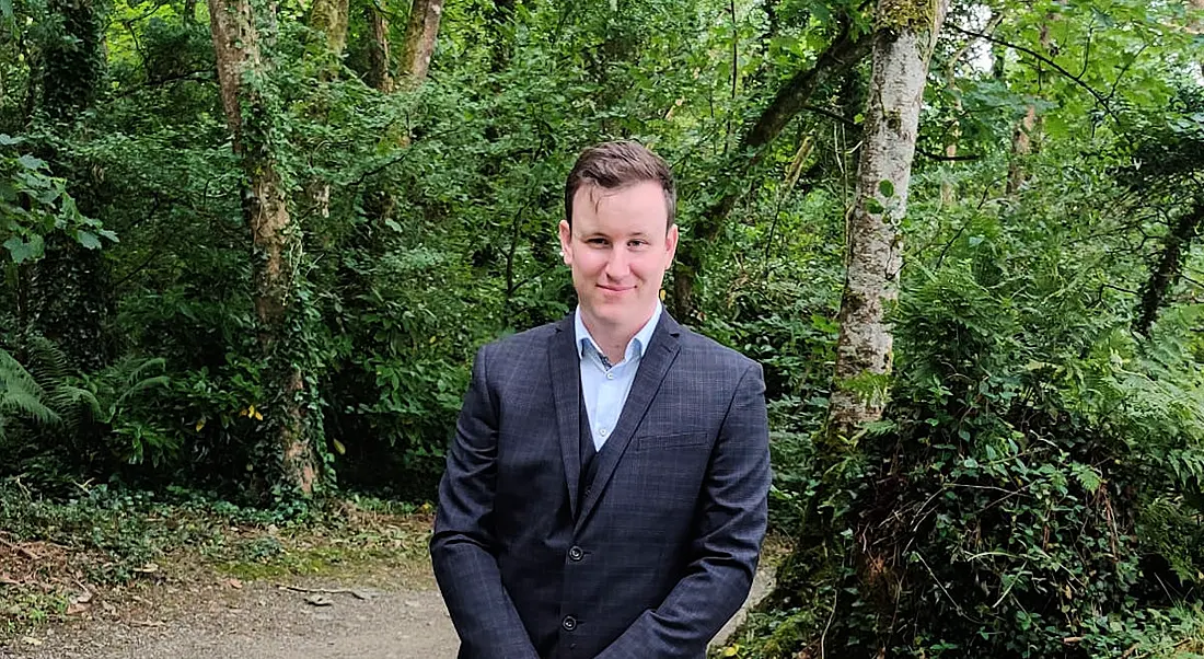 A man wearing a dark navy suit with a light blue open-collar shirt smiles in an outdoor setting. He is Sean Paterson, a senior technology engineer at Merck.