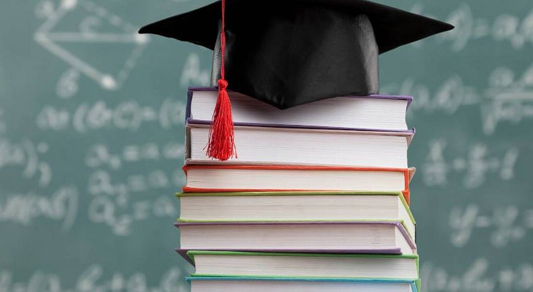 A graduate's cap sits atop a pile of books, representative of college placements and further success.