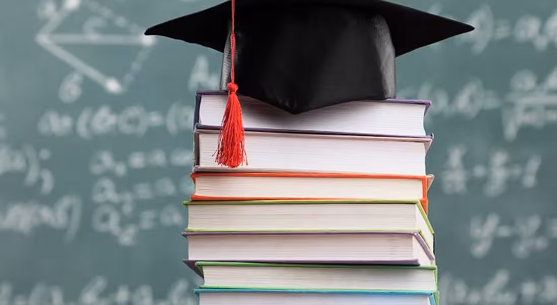 A graduate's cap sits atop a pile of books, representative of college placements and further success.