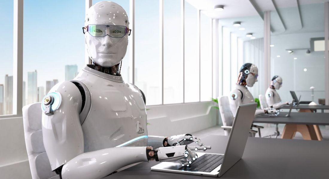 A robot, representing AI domination in the workforce, sits in an office with AI co-workers, working on a computer.