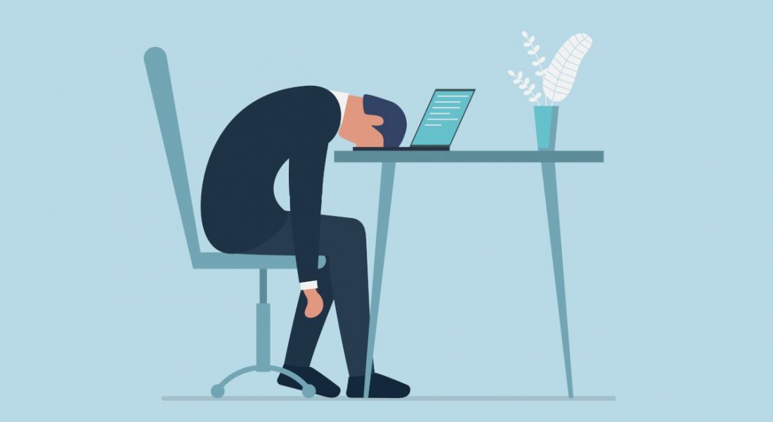 A manager is slumped over his desk and laptop, indicating he is quietly quitting, or disengaging from his work.