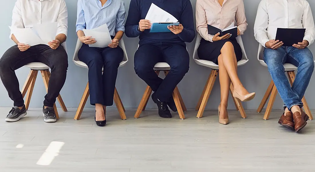 A line of people sit, with devices, to symbolise preparing for a new job or interview. The tops of their heads are not in view.