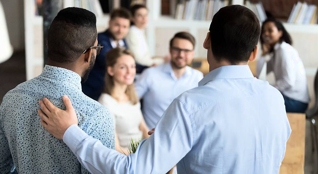 A man introduces a second man to a team, representing introduction to a new job.