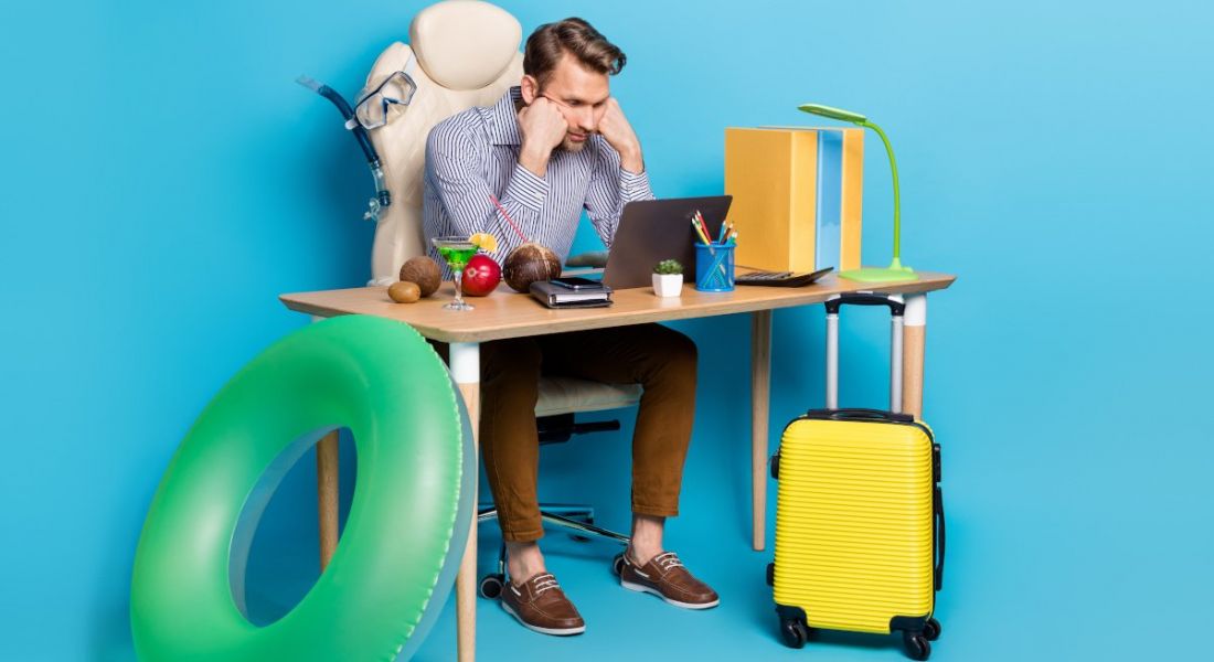 A man sits at his desk surrounded by holiday items, struggling to unplug from work.