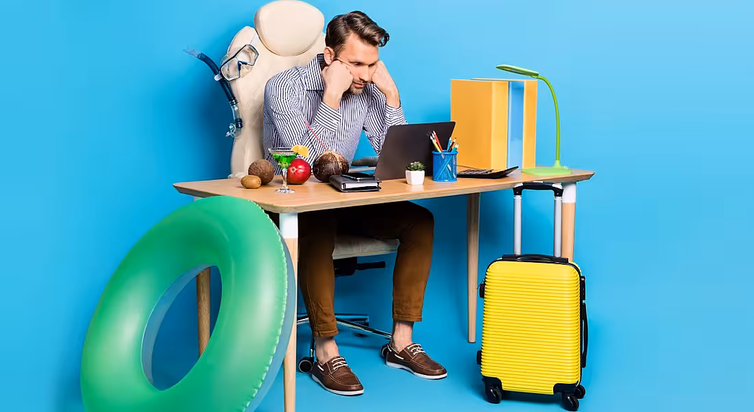 A man sits at his desk surrounded by holiday items, struggling to unplug from work.