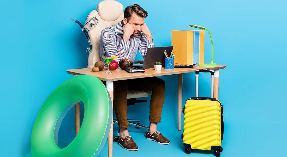 A man sits at his desk surrounded by holiday items, struggling to unplug from work.