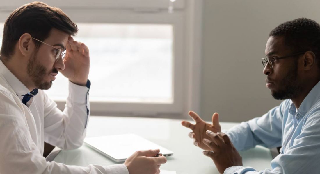 An interviewer is stressed as he speaks with an interviewee in an office.